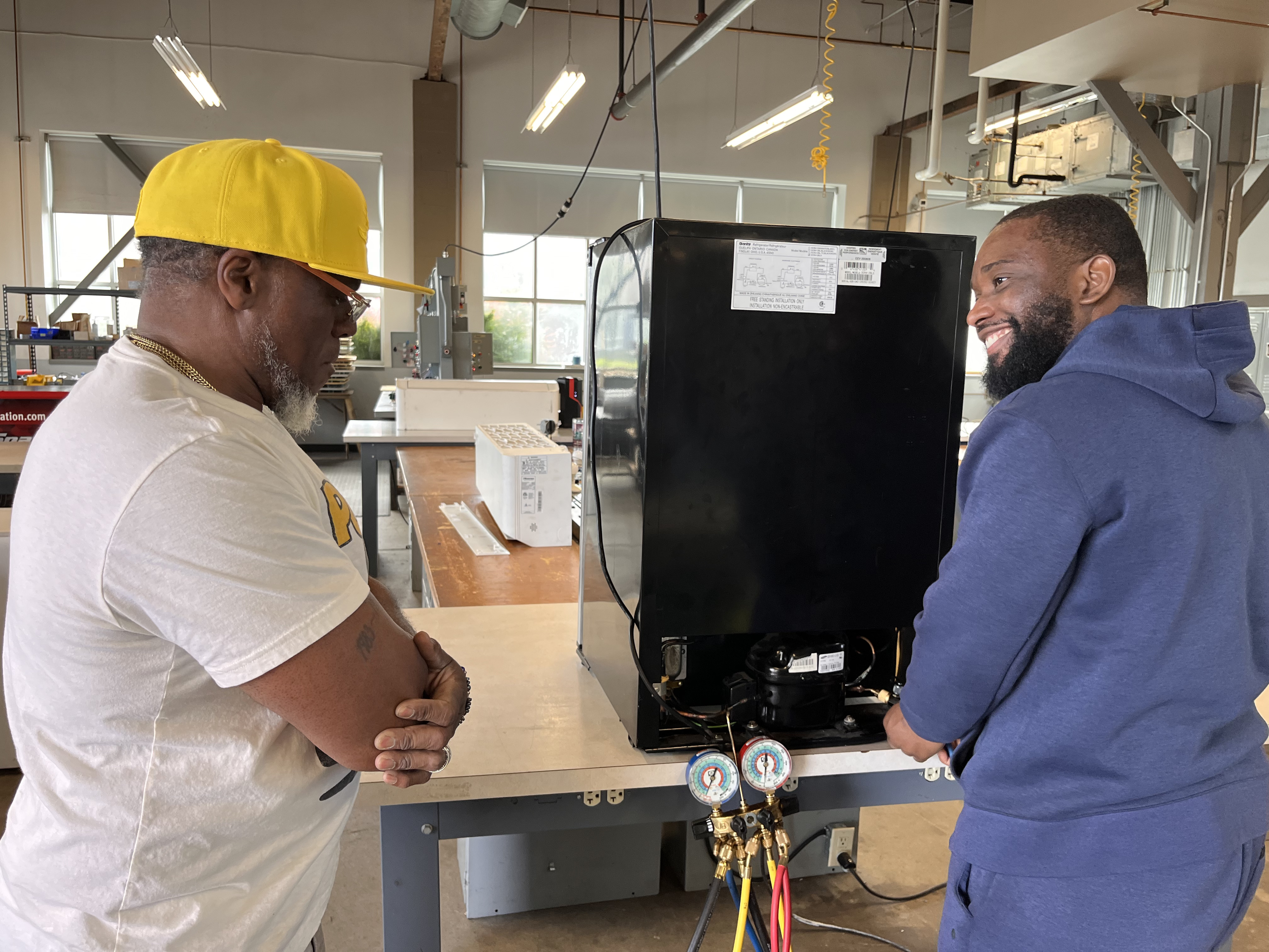 Instructor and student inspecting a refrigeration unit with manifold gauges in the training lab